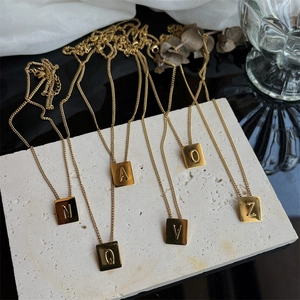 Close-up of square gold titanium steel letter pendants with delicate cross chain detail