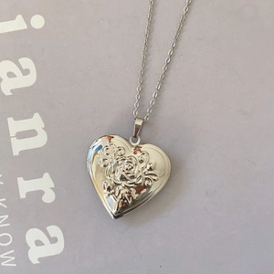 Detail of a heart-shaped locket necklace with an embossed rose on silver metal