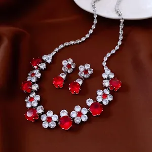 Elegant zircon flower pendant necklace and earrings set with red gems on velvet background