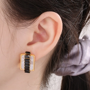 Detailed view of rectangular gold earrings with black stones and shell inlay on a model