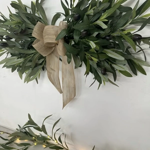 Artificial olive leaf wreath with dark berries and a burlap bow for home wall decoration
