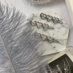 Tre fermagli per capelli in metallo argentato a forma di cuore su vassoio di marmo