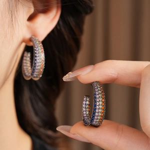 Detailed view of C-shaped earrings with colorful pave zircon stones on model ear