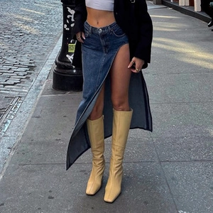 Détail d'une jupe en jean avec fente haute et bottes portées par un mannequin