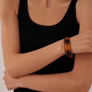 Close-up of a wide amber acrylic bangle with tortoiseshell texture on a woman's wrist