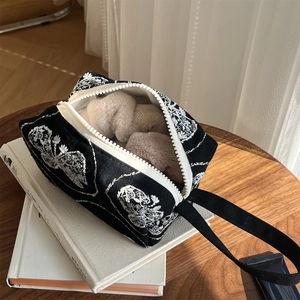Detail of black canvas bag featuring white floral embroidery and zipper on wooden desk