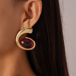 Detailed shot of an oversized golden metallic earring with a large dark red oval resin gem