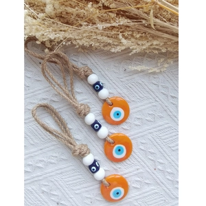 Detailed close-up of three orange Evil Eye wall charms with jute rope and beads