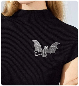Detailed view of a silver bat-winged cat brooch on a black knit sweater garment