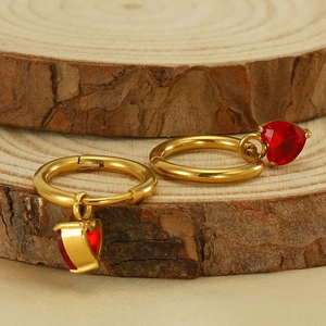 Detail of gold heart earrings with red zircon on a natural wooden background