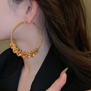 Close-up of gold oversized hoop earring with amber faceted gemstones on a female model