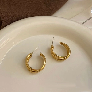 Minimalistische gedrehte goldene Creolen auf elegantem Keramikteller präsentiert