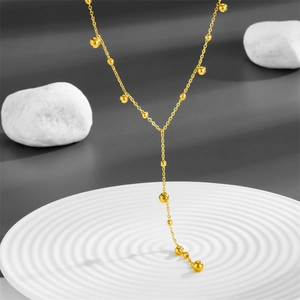 Minimalist gold Y-shaped titanium steel tassel necklace with beads on white ceramic plate