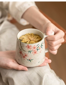 Close-up of hands holding a peach blossom ceramic mug with tea infuser inside