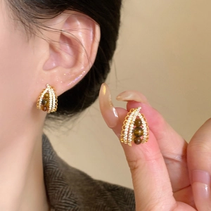Detailed view of woven gold earrings with tiger eye beads and zircon drop accents