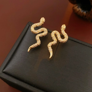 Vue macro de boucles d'oreilles serpent dorées avec zircons étincelants sur un écrin