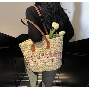 Detail of straw tote bag with colorful woven bands and brown leather straps on stairs
