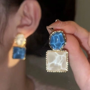 Detail showing blue and cream geometric resin earrings with elegant gold-plated edges