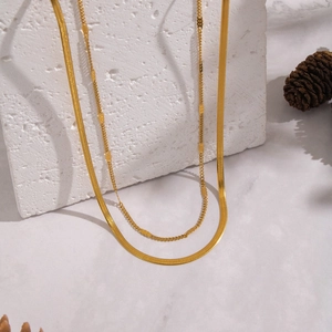 Detail of gold double-layer snake chain necklace draped over a textured stone pedestal