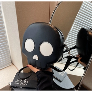 Hand holding a unique black skull shaped crossbody bag with contrast white facial details