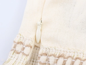Macro detail of invisible zipper on cream cotton linen fabric with tassel trim and gold thread