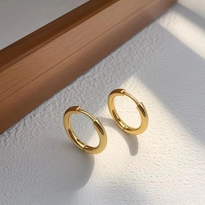 Detailed view of polished golden huggie earrings with a hinged closure on a textured surface