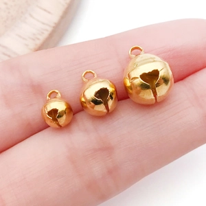 Three gold-tone vintage alloy jingle bells in various sizes held on fingertips