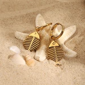 Golden stainless steel fishbone earrings displayed on a beach with starfish and shells