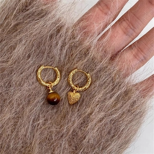 Détails des créoles plaquées or avec des breloques asymétriques en oeil de tigre et coeur