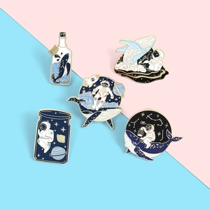 Detail of five enamel pins with astronaut and whale motifs in deep blue and gold