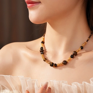 Détail des perles d'oeil de tigre et chaîne dorée torsadée sur le cou du mannequin