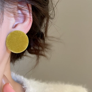 Close-up of mustard yellow flocked button earrings worn on ear showing soft velvet texture