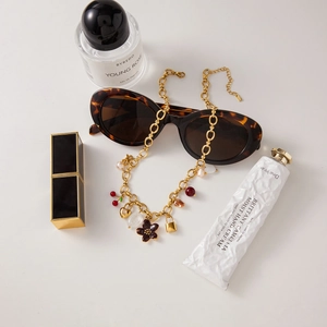 Detail of gold pearl necklace with red flower, heart, and padlock charms on white background