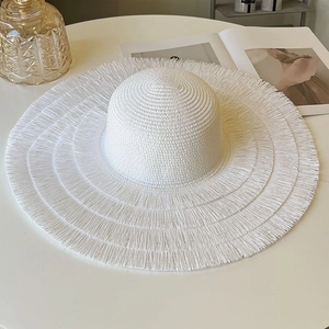 Close-up of white straw sun hat with layered fringe brim on minimalist white table