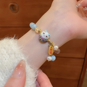 Detail of beaded bracelet with ceramic Maneki-Neko charm and gold blessing tag