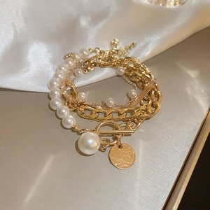 Detail of layered gold metal chain bracelet with pearls and toggle clasp on silk
