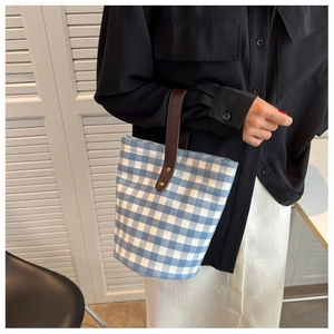 Detailed view of canvas bucket bag with blue and white check pattern and leather handle