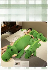 Détail de trois tailles d'oreillers en peluche crocodile verte posés sur un lit douillet