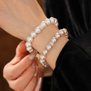 Vue détaillée de bracelets en perles blanches superposés avec fleur en zircon au poignet
