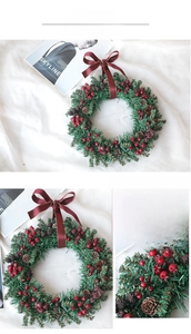 Detailed view of handmade Christmas wreath with pine cones and red berries on white fabric