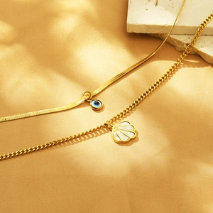 Detail of gold snake chain with blue evil eye and shell pendants on natural stone