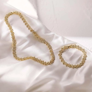 Gold-toned leaf jewelry set with crystal necklace and bracelet on white silk fabric
