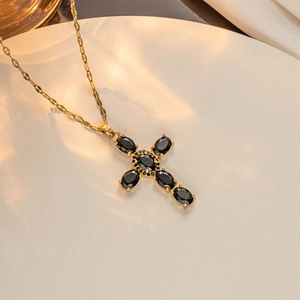 Close-up of gold-plated cross necklace with oval black zircon stones on silk fabric