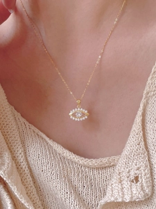 Close-up of a gold evil eye pendant necklace with cubic zirconia on a model