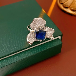 Detailed close-up of a zircon flower ring with a square blue gemstone on a jewelry box
