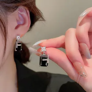 Detail of silver earring featuring a square zircon and black gemstone with an F letter