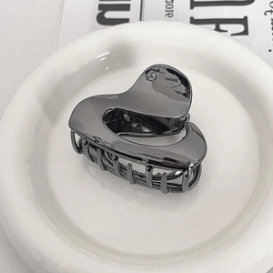 Detail view of a hollow heart-shaped metal hair claw in gunmetal grey finish on a plate