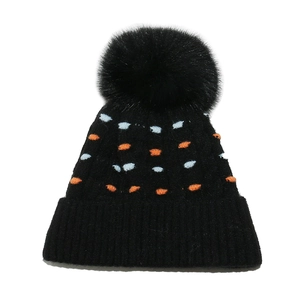 Gorro de punto invernal con pompón grande y lunares de colores sobre tejido de lana negra