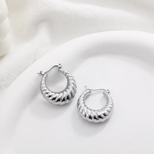 Macro shot of silver twisted rope textured hoop earrings on white ceramic tray