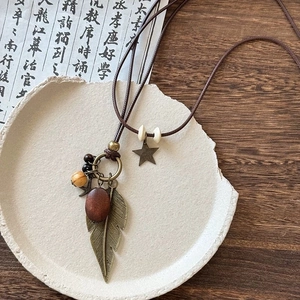 Bohemian floral pendant necklace with bronze feathers and wooden beads on a ceramic plate